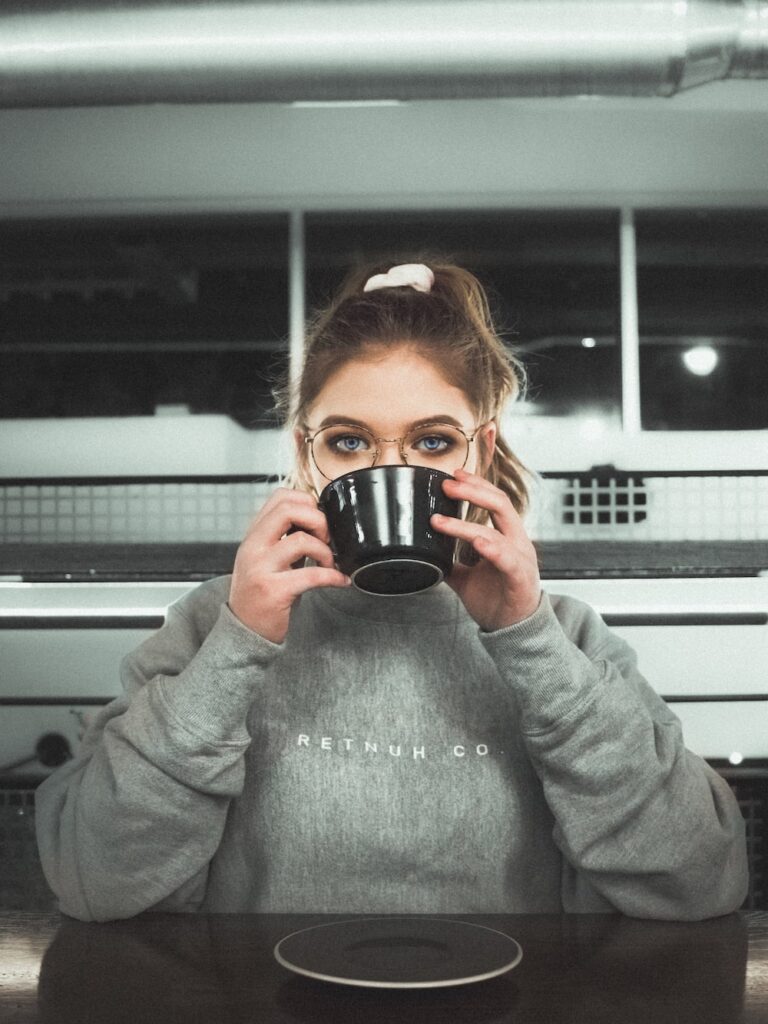 A woman drinking while wearing a sweatshirt